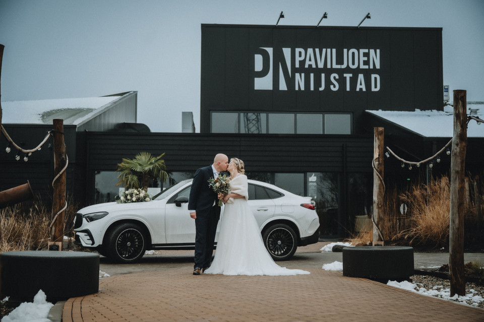 een bruid en bruidegom die voor een witte auto staan met een zwart bord dat zegt paul queen nilistad