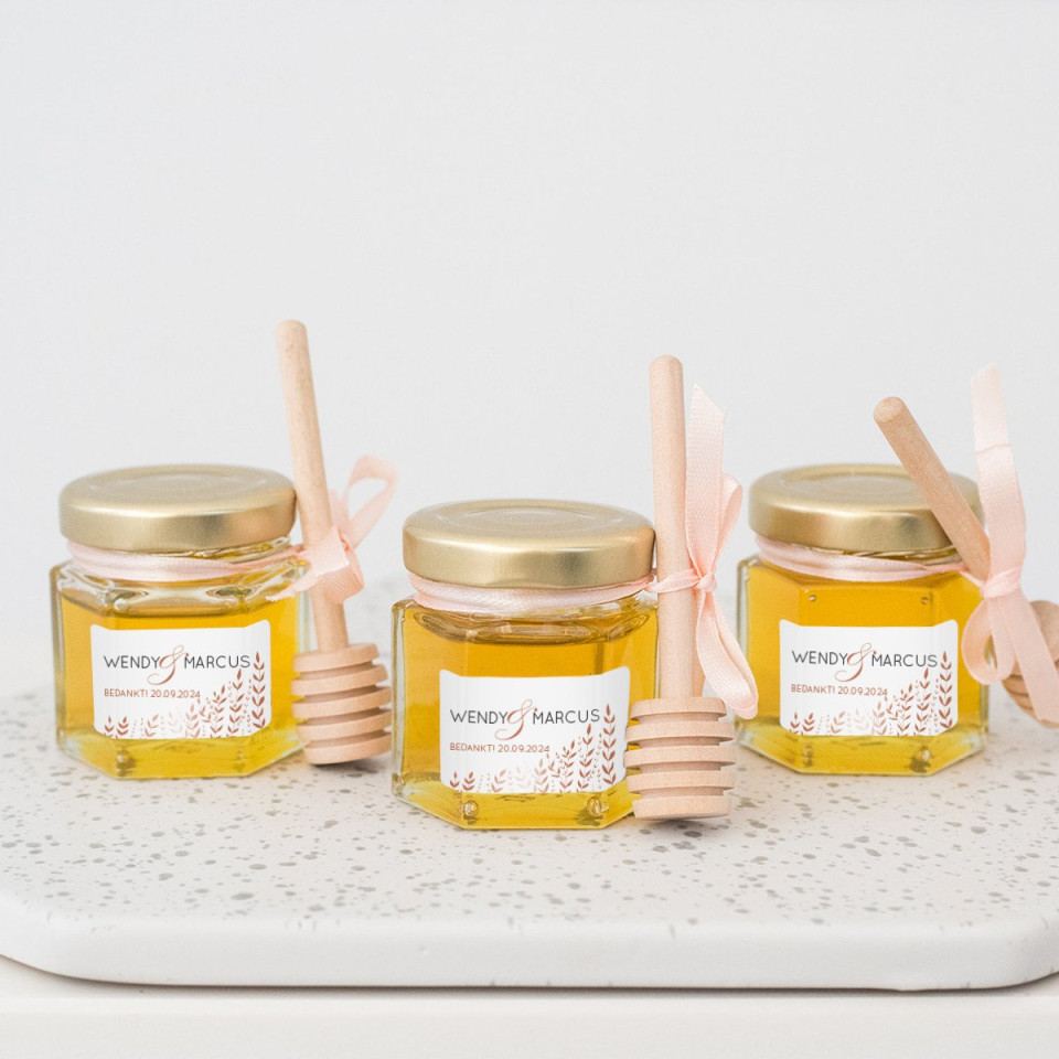 drie potten honing met houten stokjes op een wit dienblad