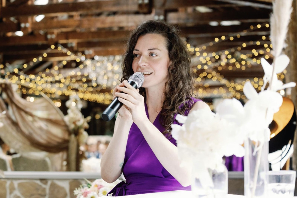 een vrouw in een paarse jurk die in een microfoon spreekt