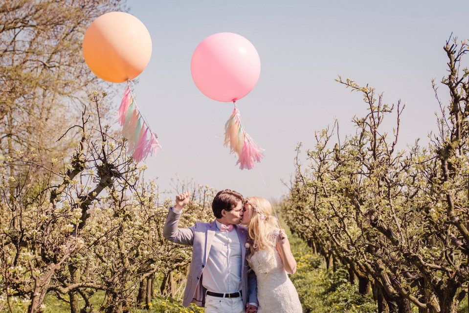 een bruid en bruidegom in een boomgaard met roze en oranje ballonnen