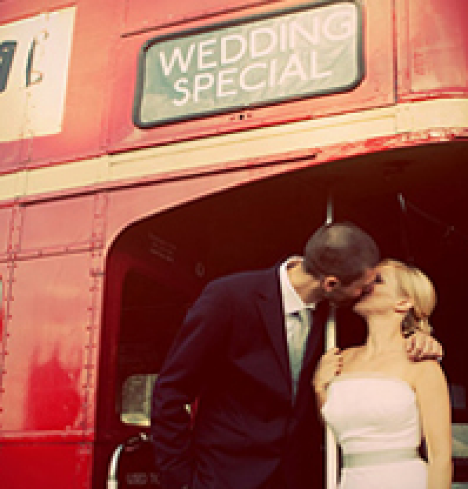 een bruid en bruidegom die kussen voor een rode dubbeldekkerbus