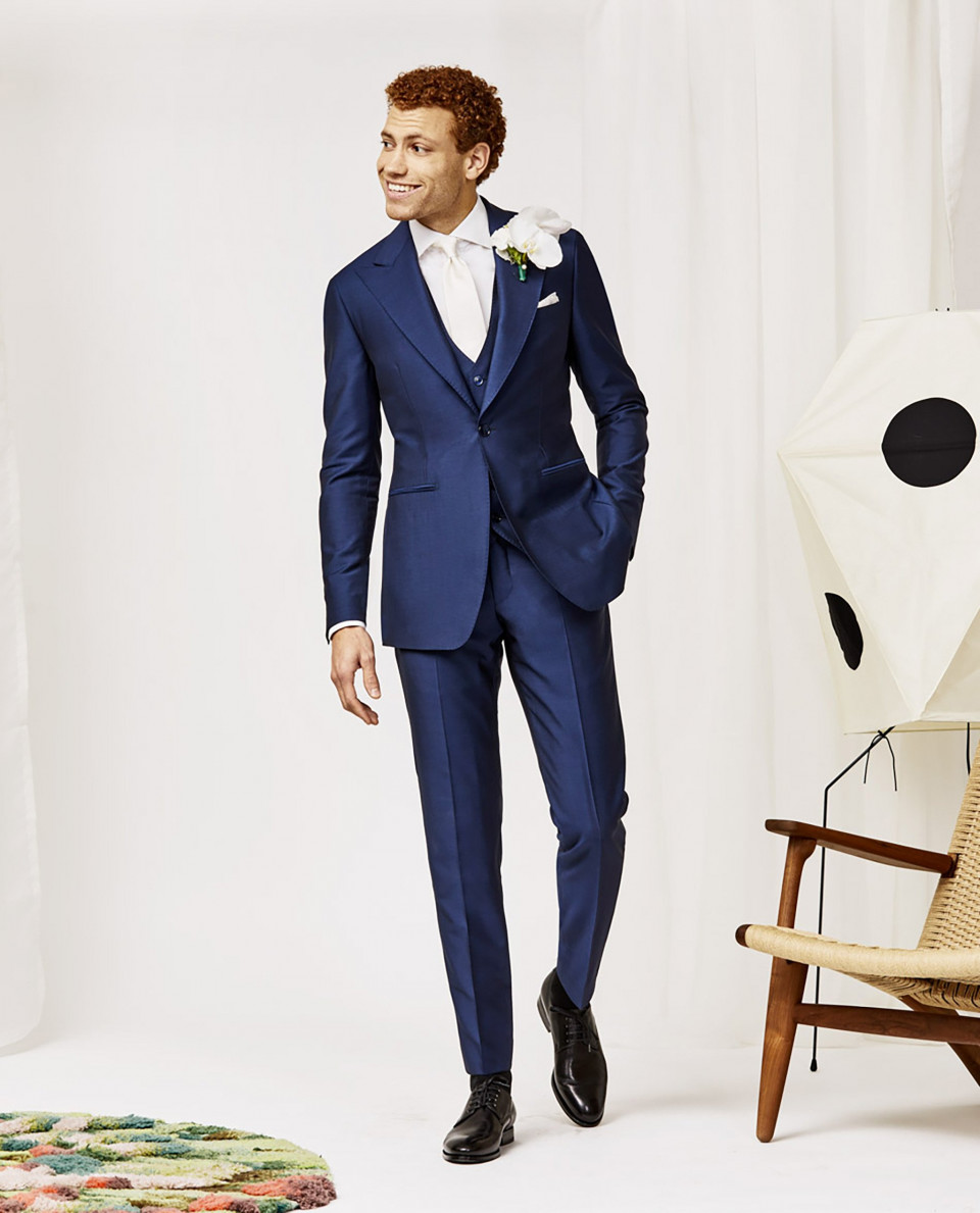 een man in een blauw pak en stropdas staat voor een stoel