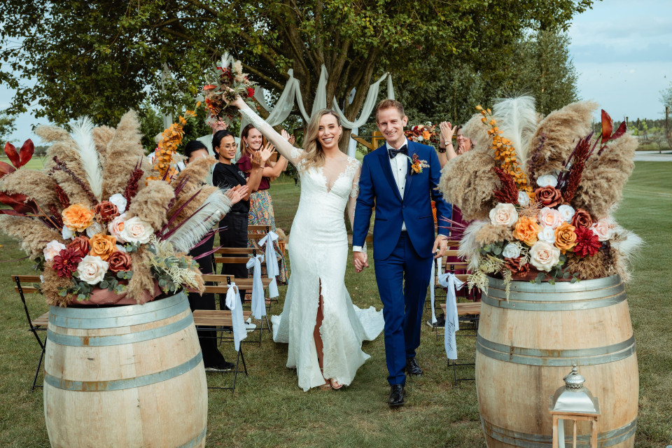 een bruid en bruidegom die met hun armen in de lucht het pad aflopen