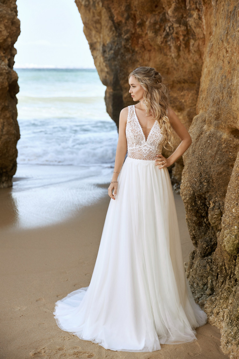 een bruid die voor een rotsformatie op het strand staat