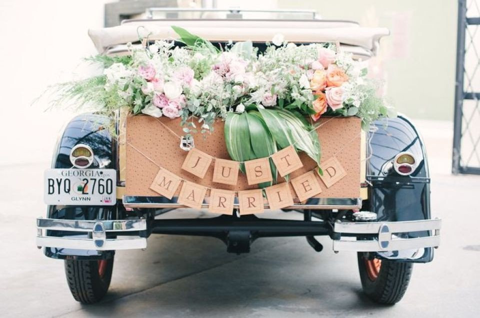 een vintage auto met bloemen en een bord met just married