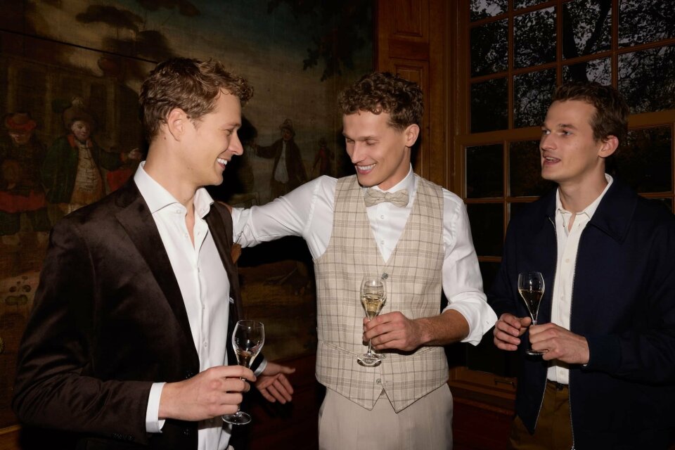 een paar mannen die naast elkaar staan met wijnglazen in hun hand