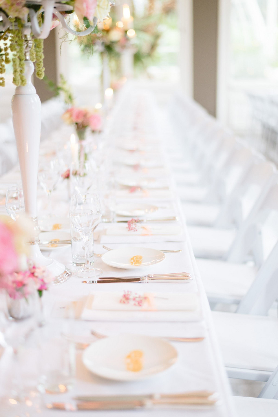een lange tafel met witte stoelen en roze bloemen