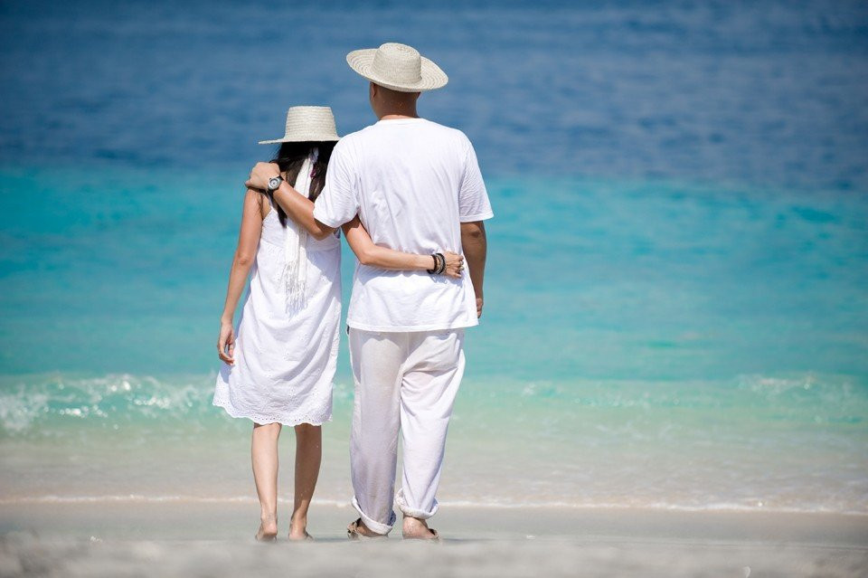 een man en vrouw in het wit lopen op het strand
