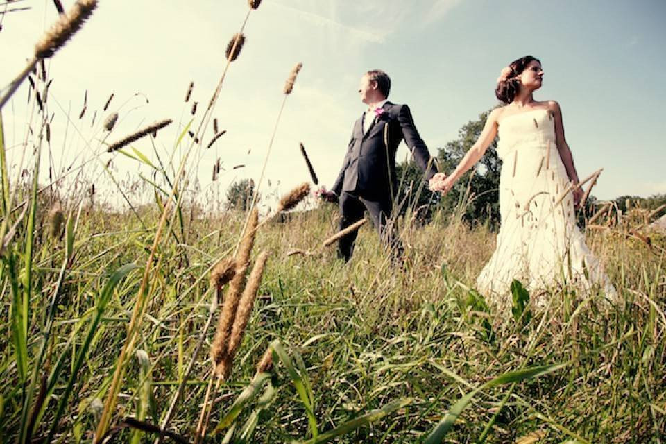 een bruid en bruidegom lopen door hoog gras