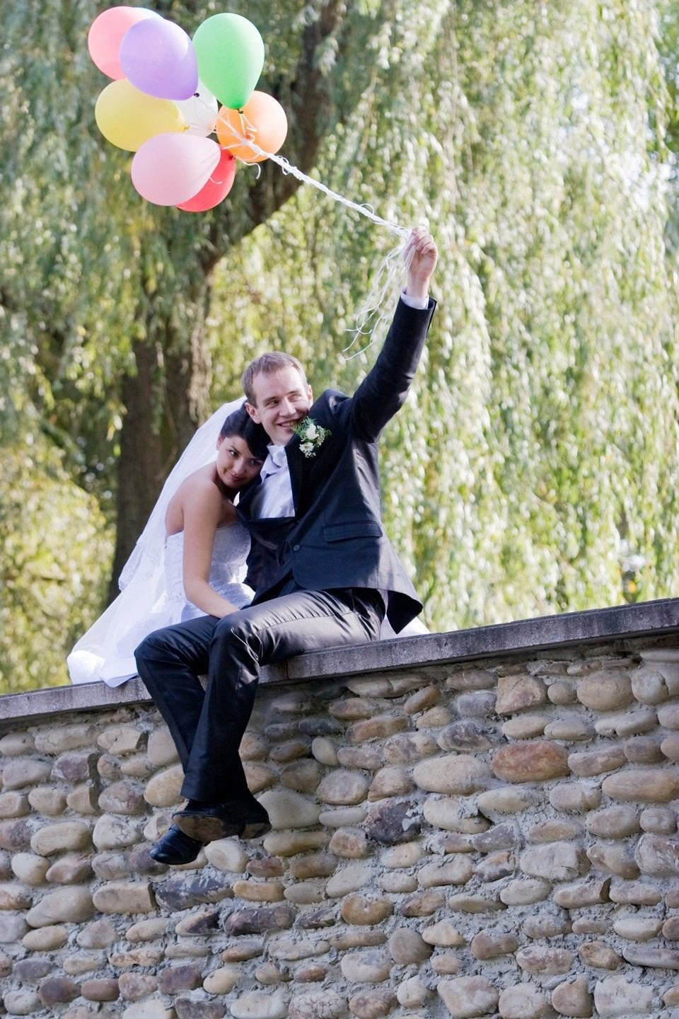 een bruidspaar zittend op een stenen muur met ballonnen
