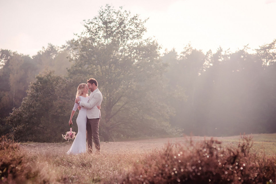 een bruid en bruidegom omhelzen elkaar in een veld bij zonsondergang