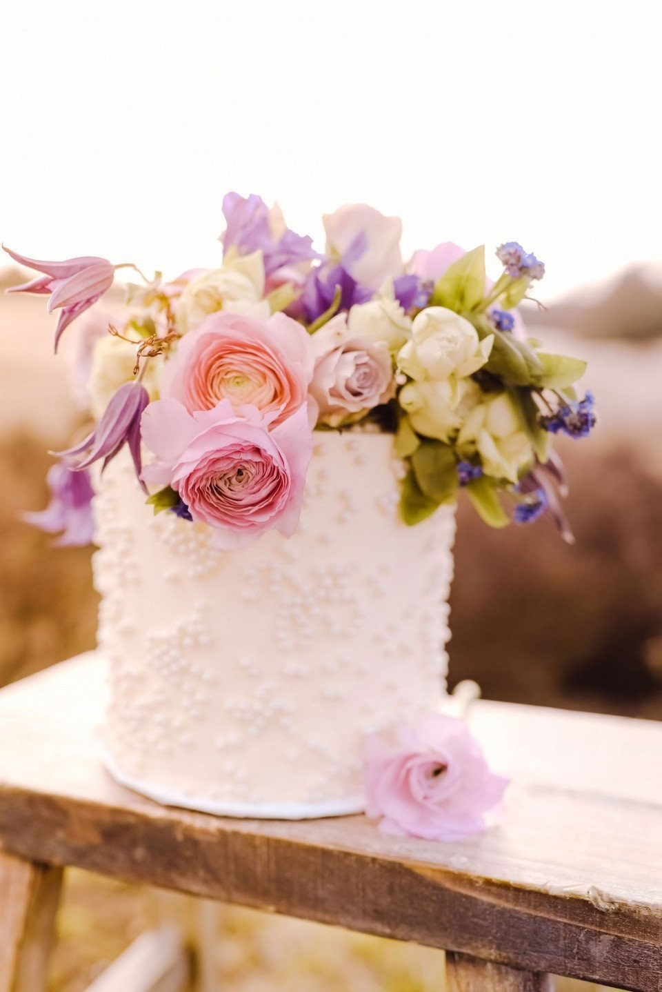 een witte taart met roze en paarse bloemen erop