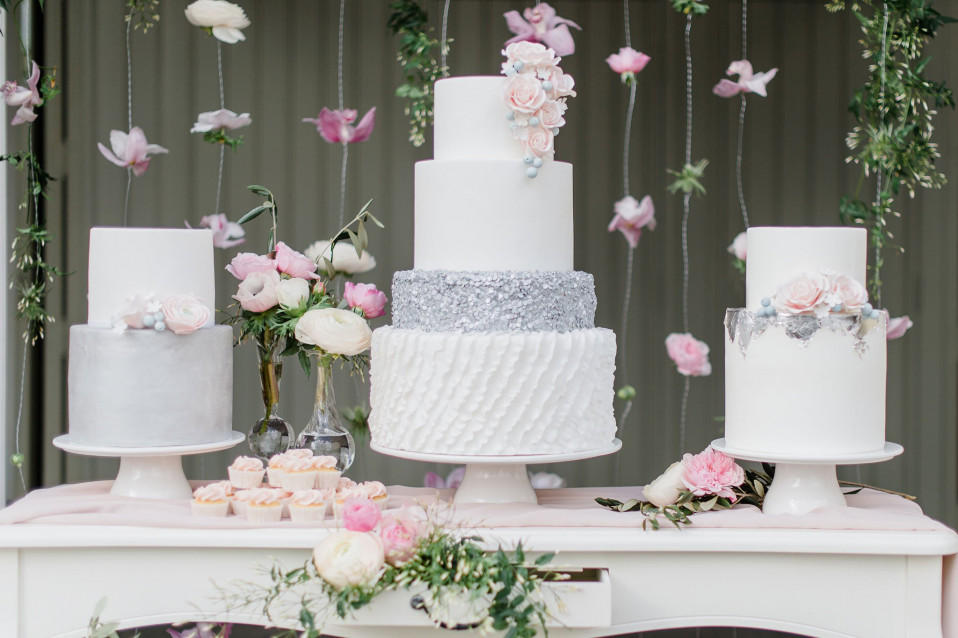 een tafel met drie bruidstaarten en bloemen