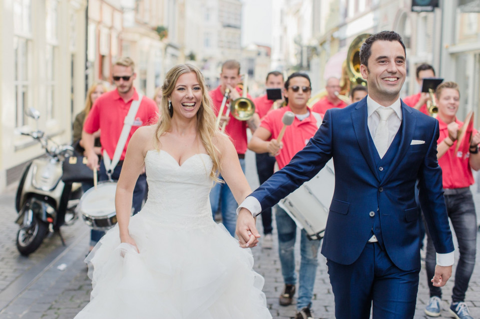 een bruid en bruidegom die door een straat lopen met een band