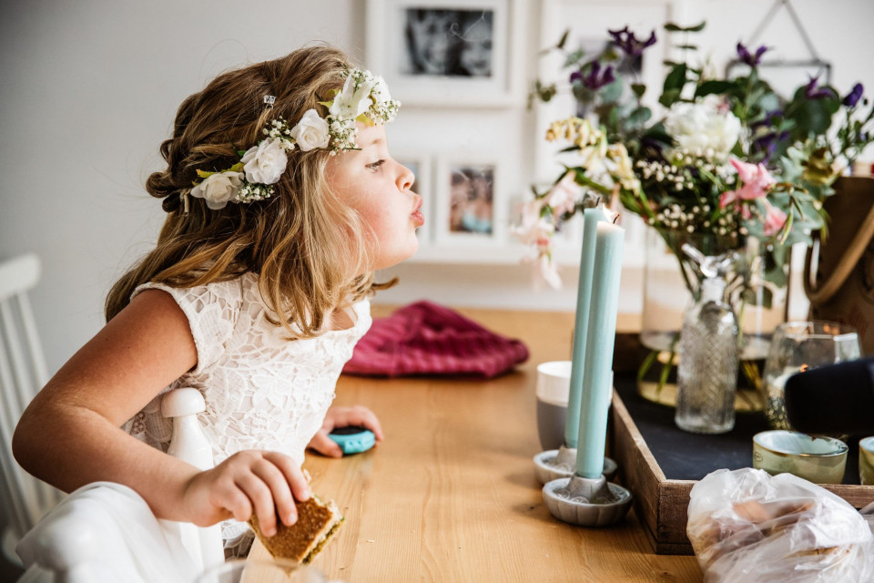 een klein meisje met een bloemenkrans zit aan tafel met bloemen