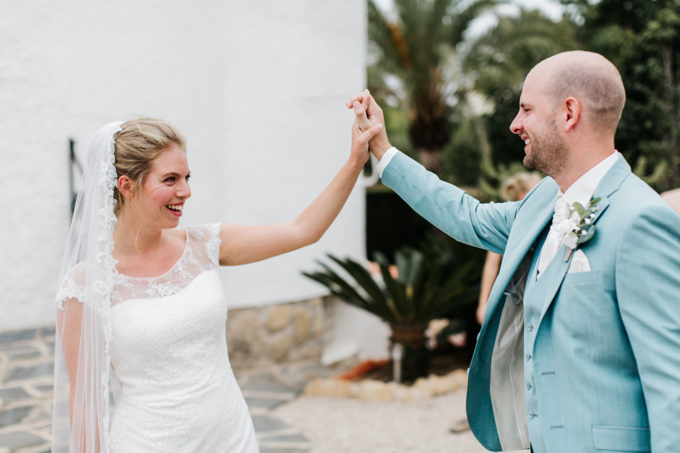 een bruid en bruidegom houden elkaars handen vast voor een wit gebouw