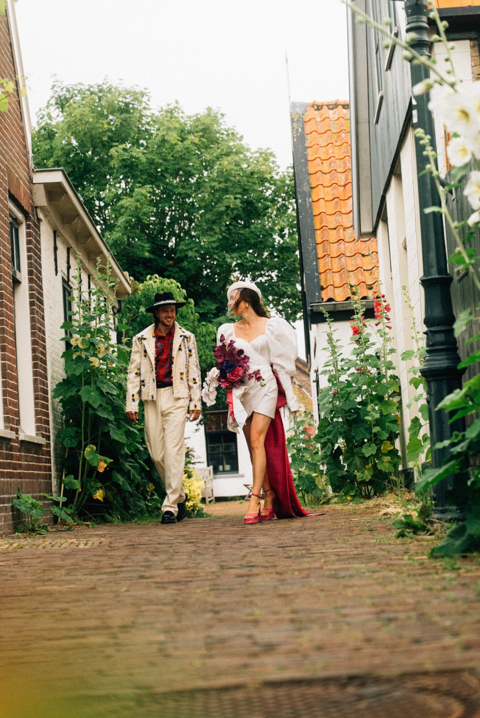 een bruid en bruidegom die een kinderkopjesstraat aflopen
