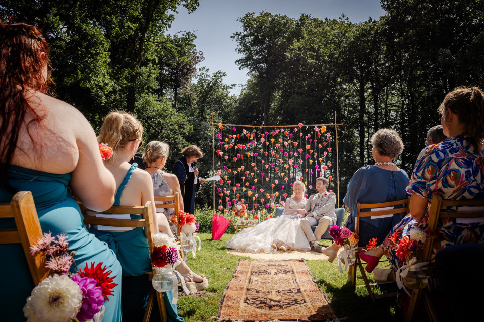 een bruiloftsceremonie in het bos met mensen die op stoelen zitten