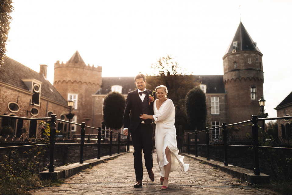 een bruid en bruidegom lopen over een kasseien pad voor een kasteel