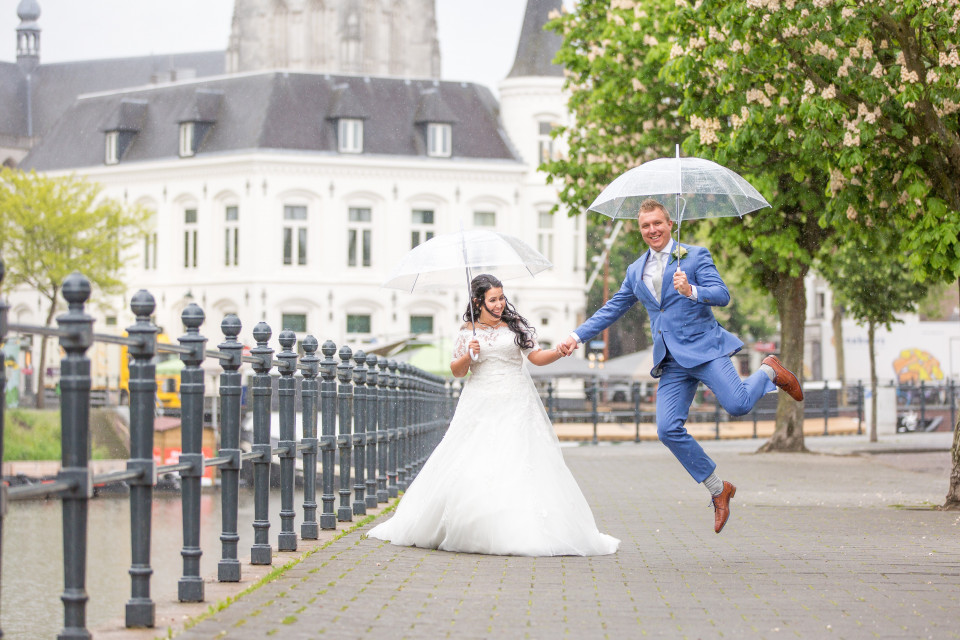 een bruid en bruidegom die in de lucht springen met paraplu's