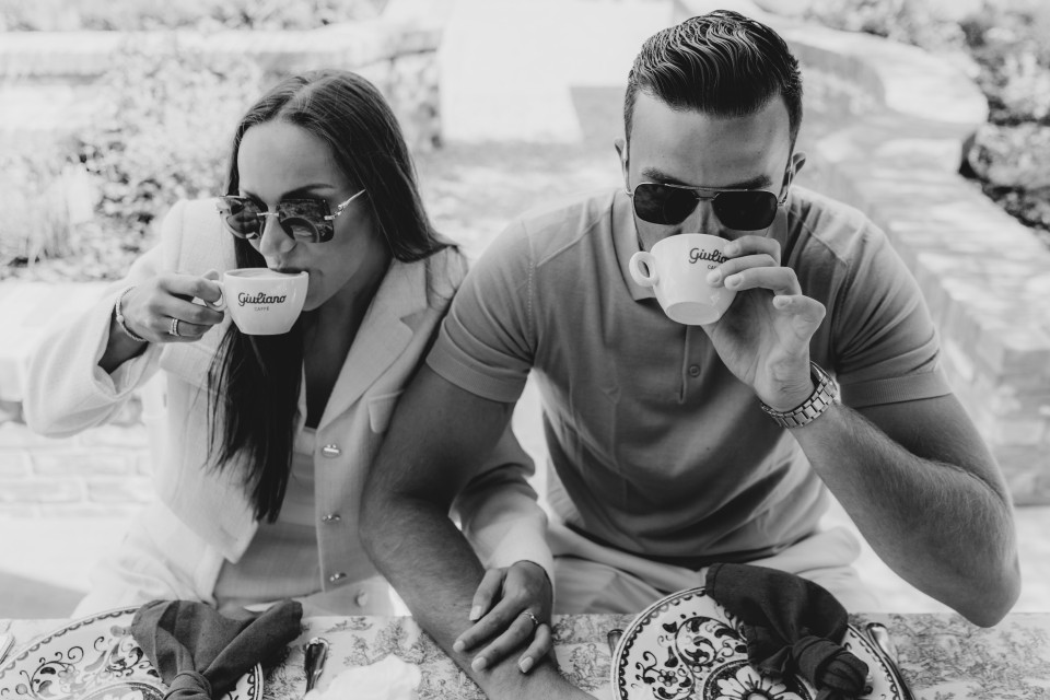een zwart-wit foto van een man en een vrouw die op een bed zitten en koffie drinken en donuts eten