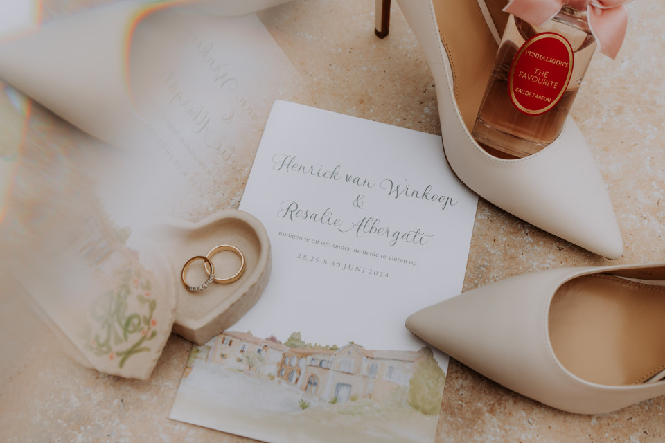 een foto van een paar schoenen en een fles parfum op de vloer naast een huwelijkskaart en ring