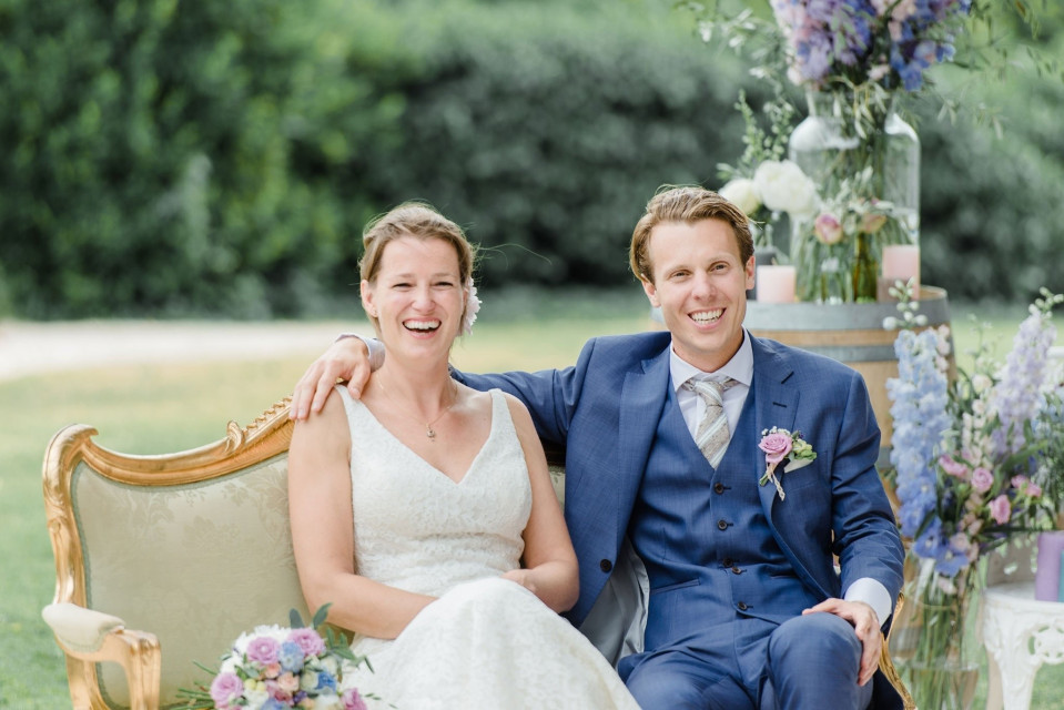 een bruid en bruidegom zitten op een stoel voor een bloemstuk