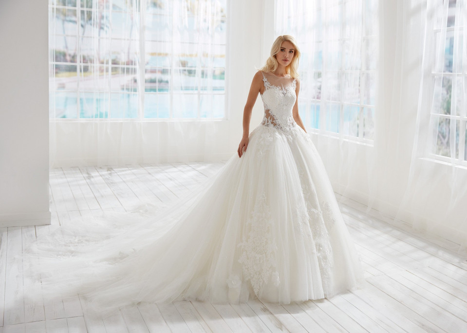 een mooie bruid in een bruidsjurk die staat in een witte kamer