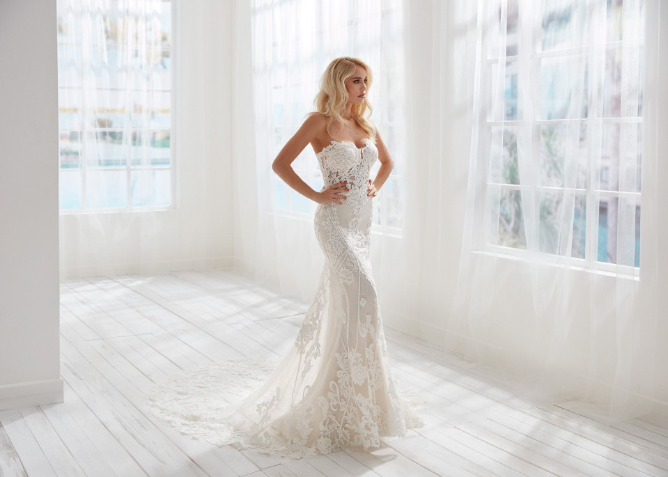 een mooie blonde vrouw in een bruidsjurk die staat voor een raam