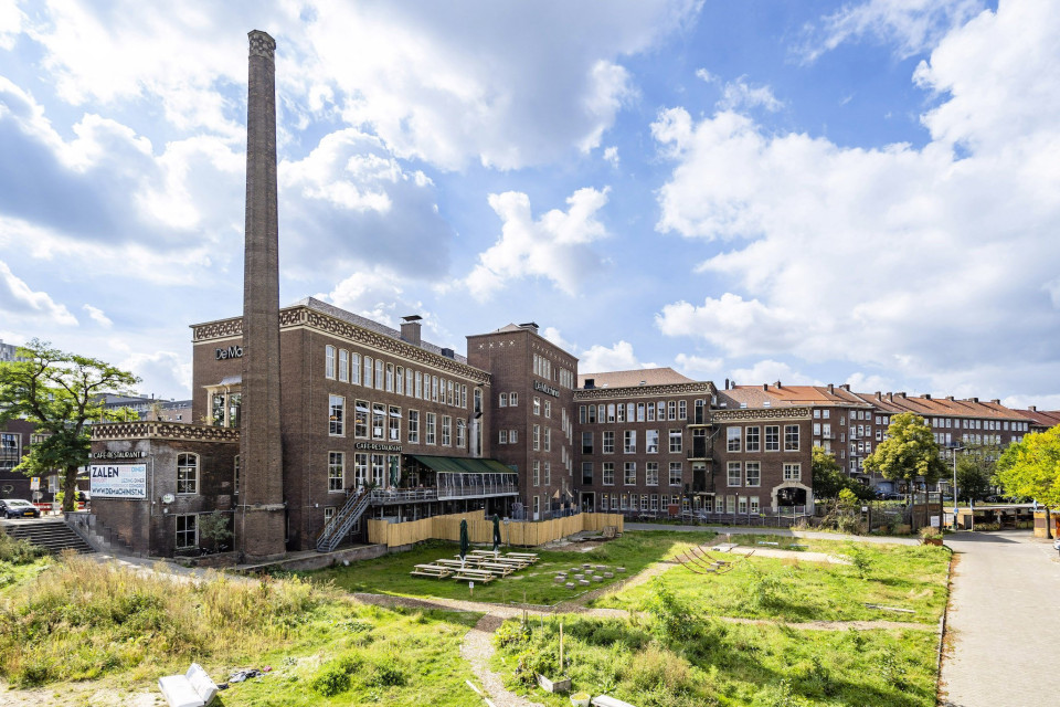 een groot bakstenen gebouw met een schoorsteen op de achtergrond