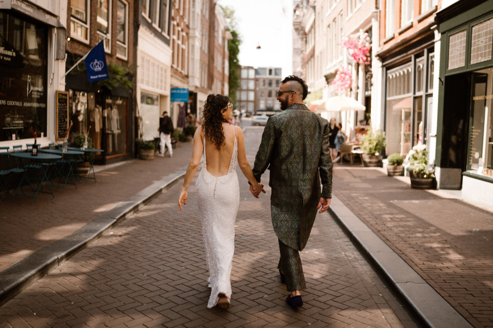 een bruid en bruidegom lopen door een smalle straat in Amsterdam