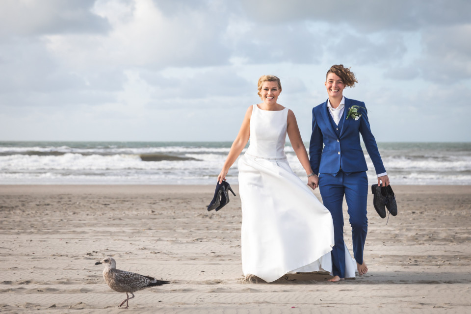 een bruid en bruidegom lopen op het strand met zeemeeuwen