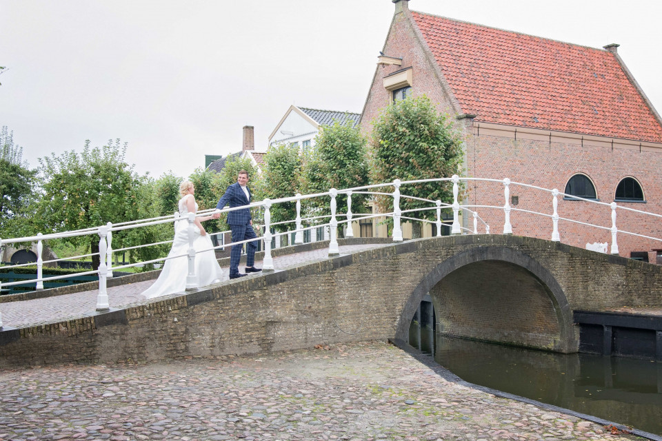 een bruid en bruidegom staan op een brug over een gracht