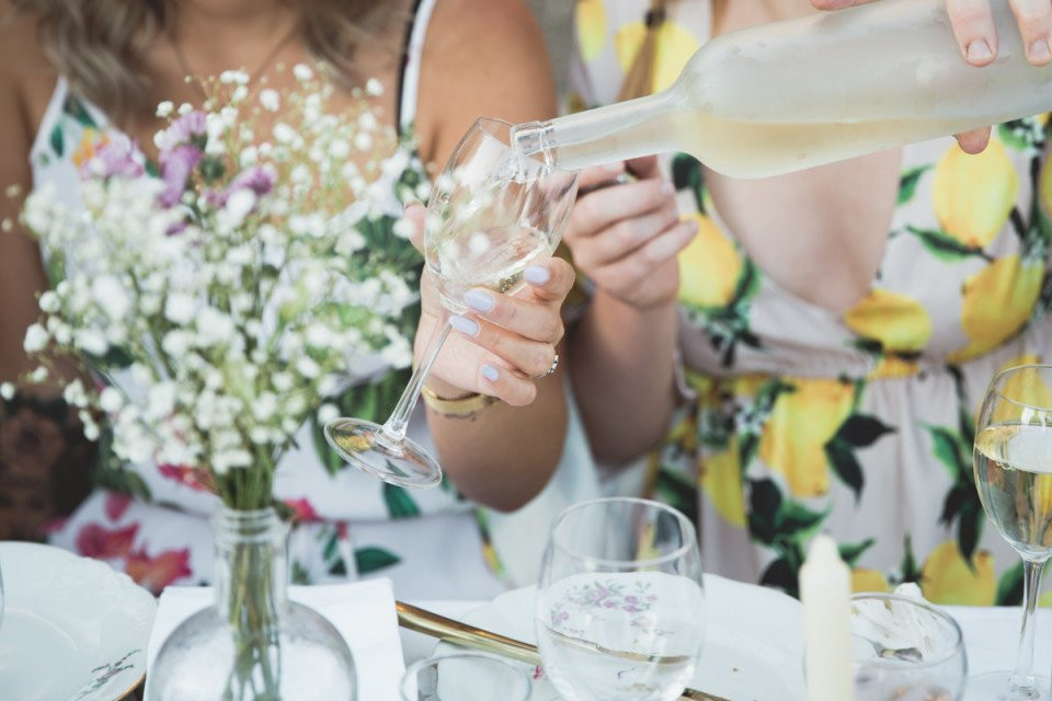 twee vrouwen schenken wijn in glazen aan een tafel