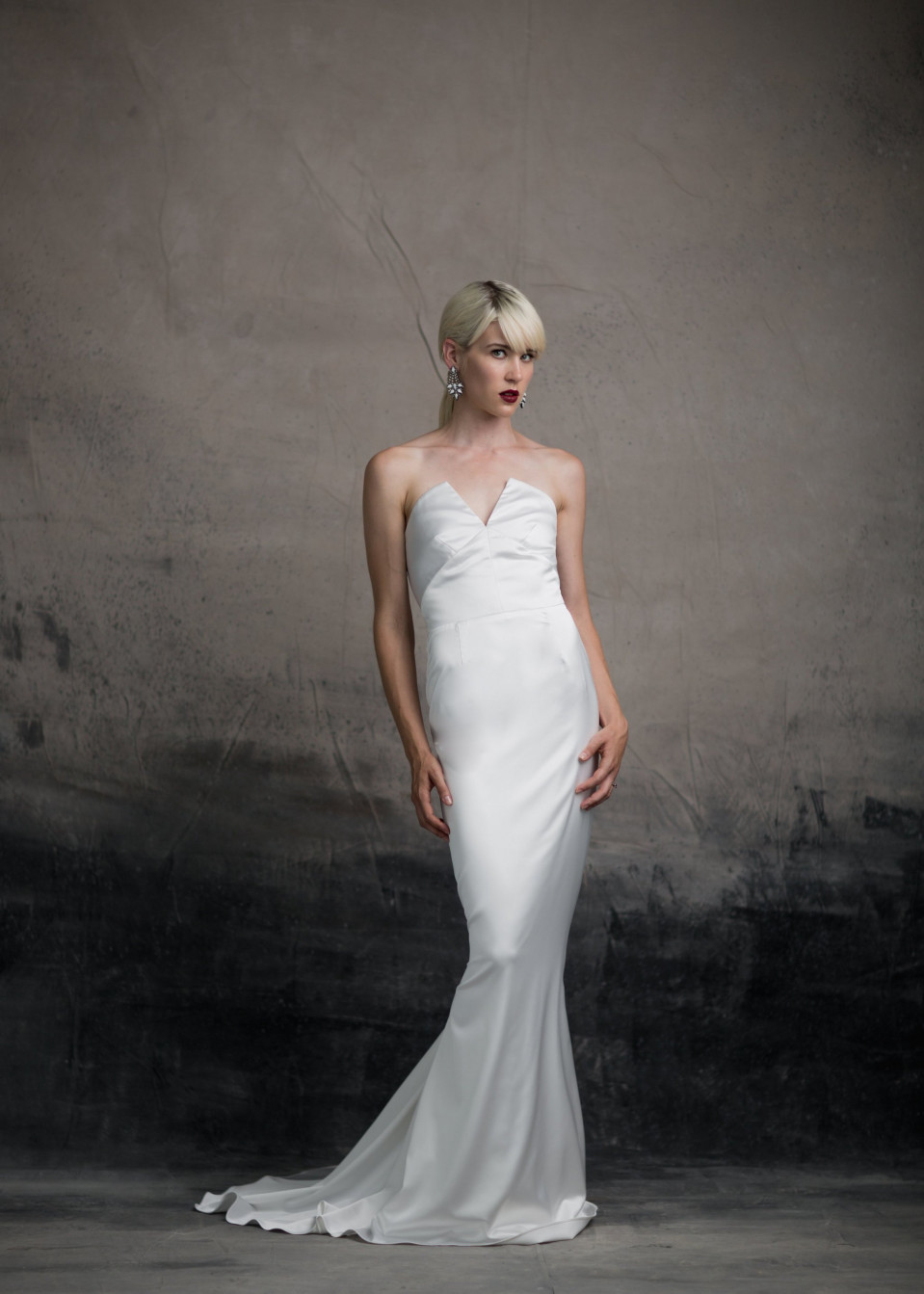 een vrouw in een witte trouwjurk staat voor een muur