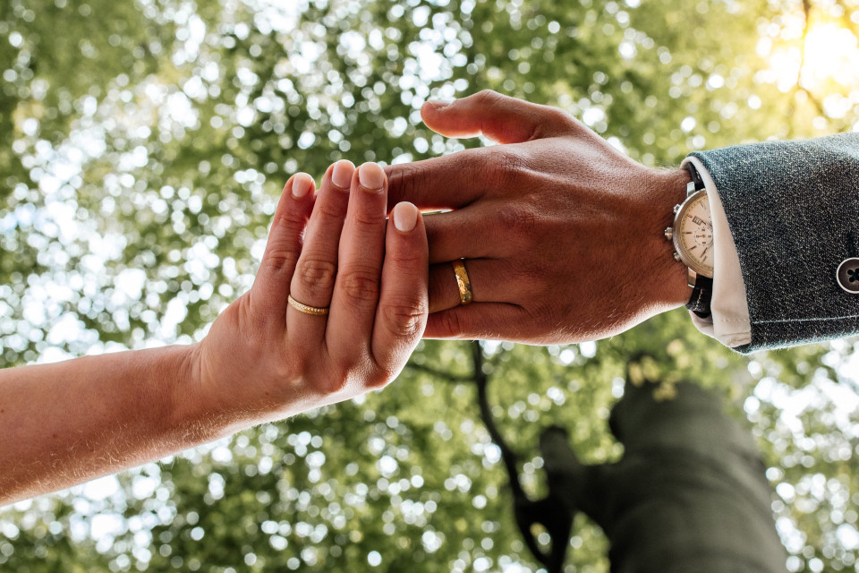 een man en vrouw die hand in hand staan voor bomen
