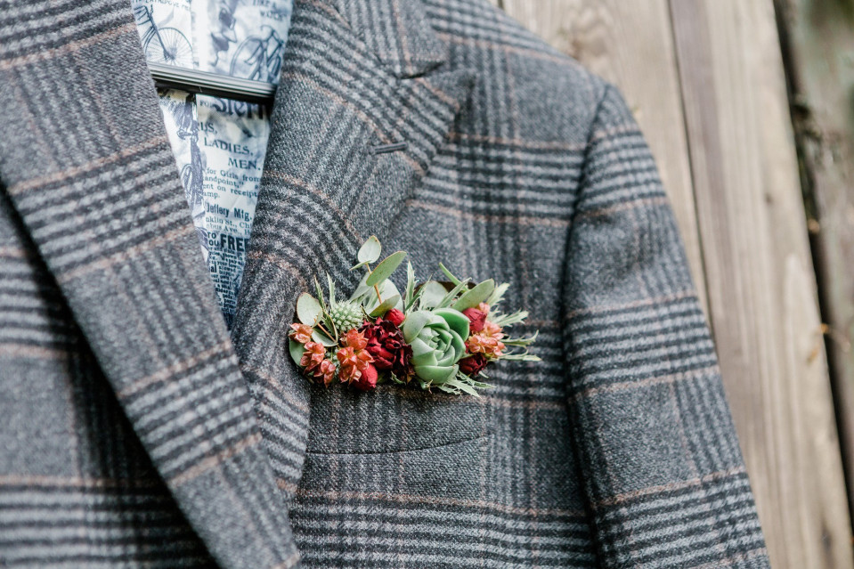 een grijs pak met een geruit overhemd en een bloemenboutonnière