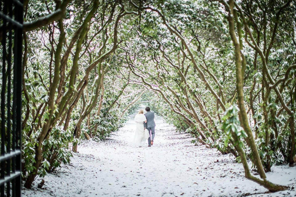 een bruid en bruidegom lopen door een tunnel van bomen