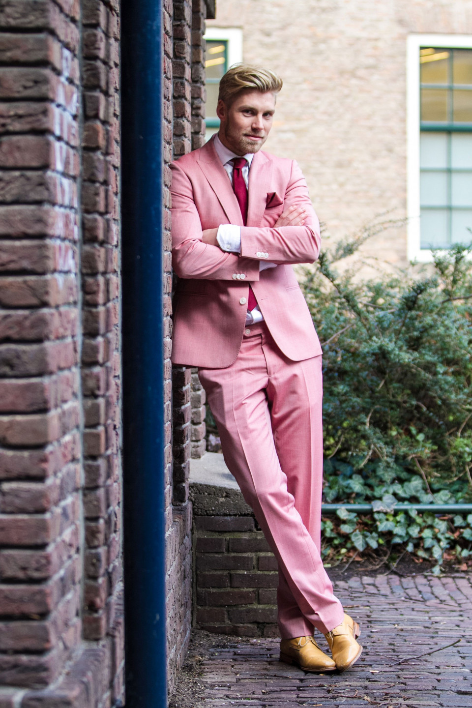 een man in een roze pak leunend tegen een bakstenen muur