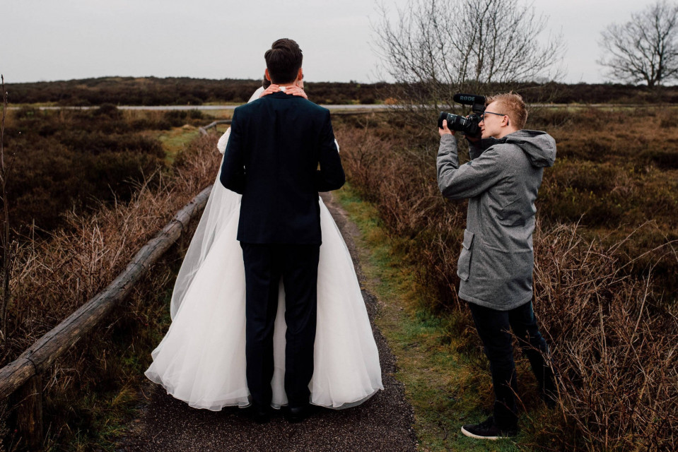 een man die een foto maakt van een bruid en bruidegom op een pad
