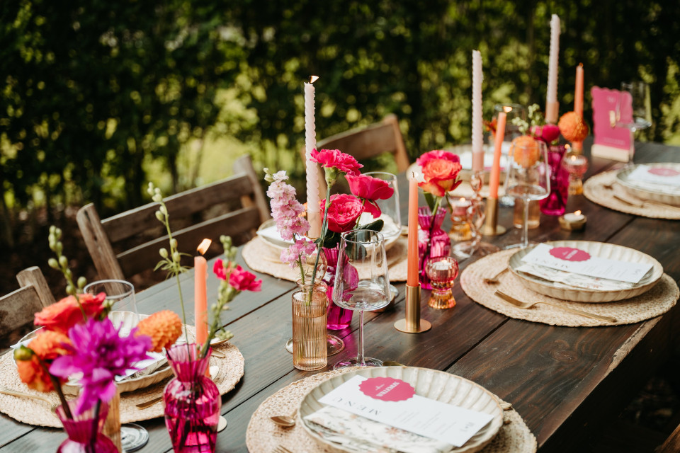 een tafel gedekt met roze en oranje bloemen en kaarsen
