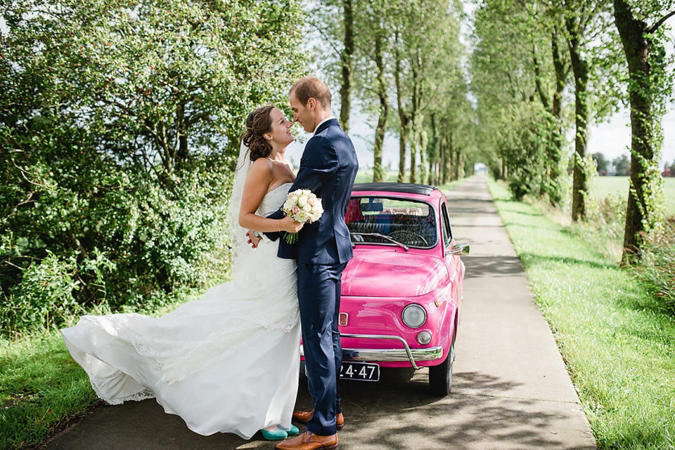 een bruid en bruidegom poseren met een roze auto