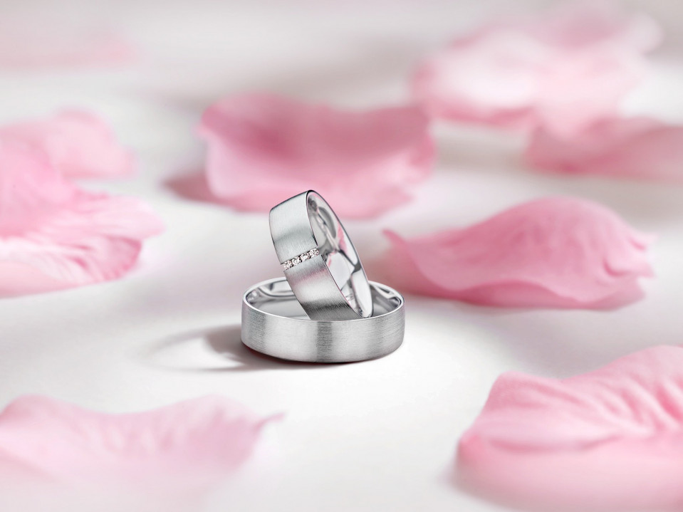 twee trouwringen op een witte achtergrond met roze bloemblaadjes