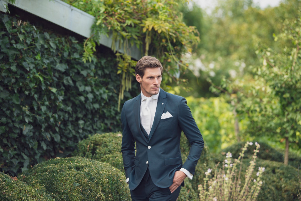 een man in pak en stropdas staat in een tuin