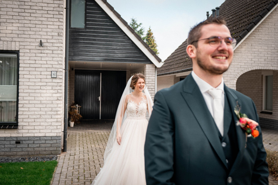 een man en vrouw in trouwkledij staan voor een huis
