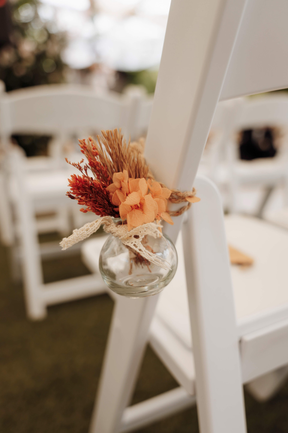 een arrangement van bloemen in een glazen vaas op de achterkant van een witte stoel