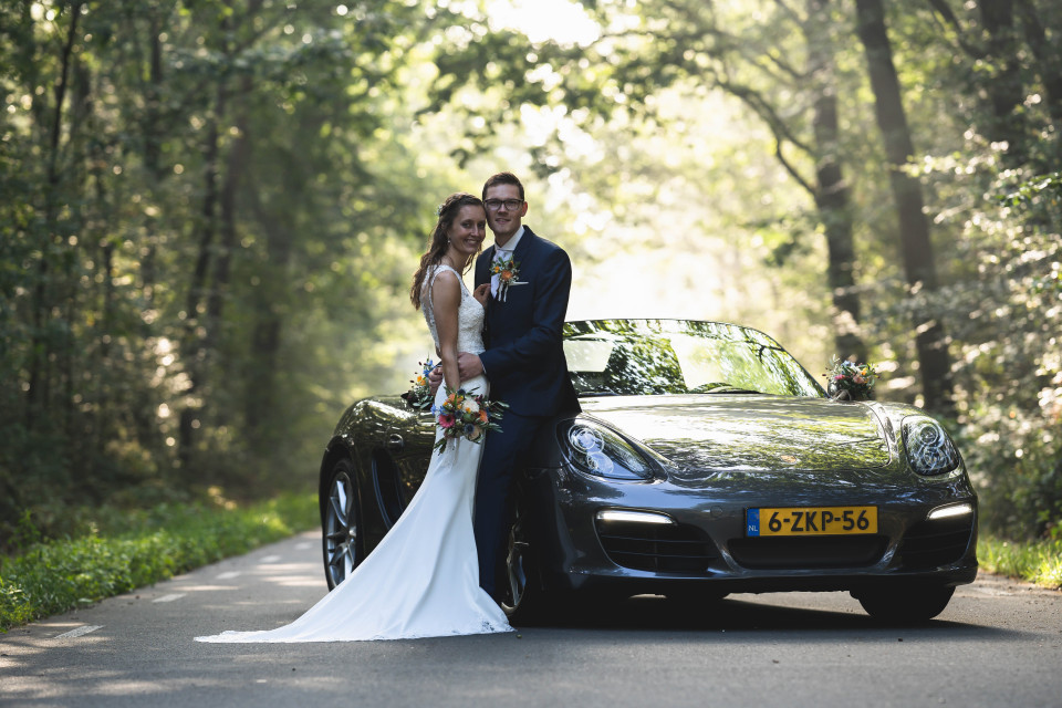 een bruid en bruidegom poseren voor een zwarte sportwagen