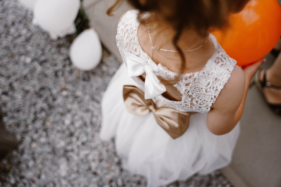 een klein meisje in een witte jurk met oranje ballonnen