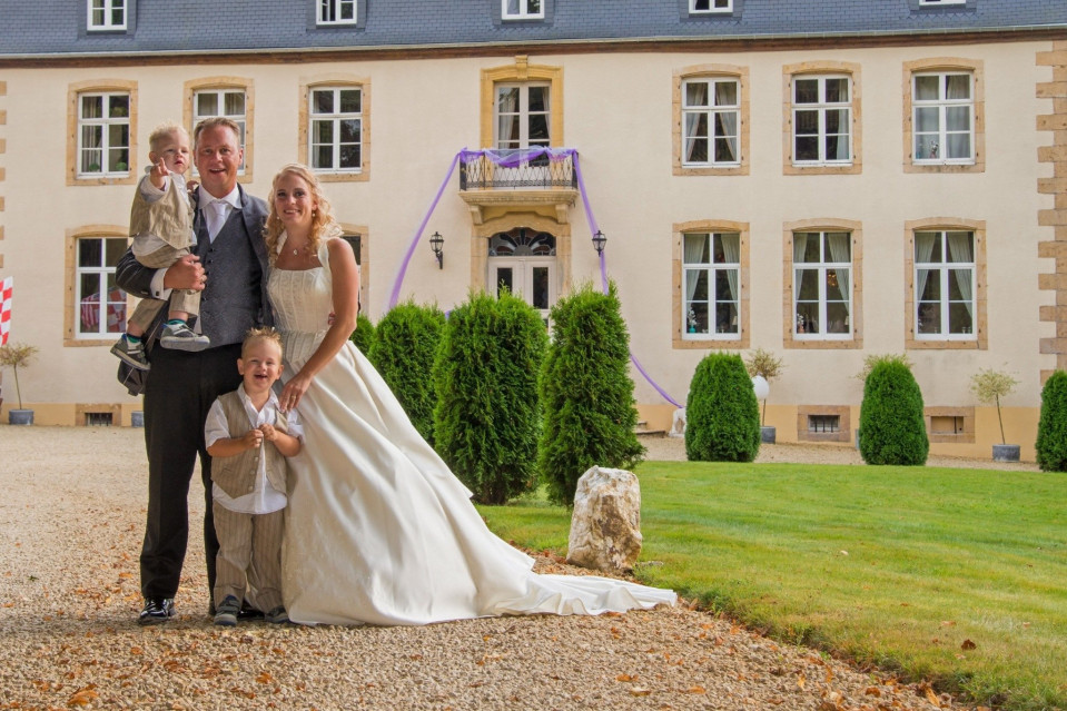 een bruid en bruidegom poseren met hun twee kinderen voor een groot landhuis