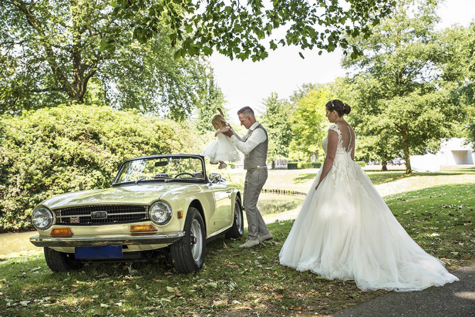 een bruid en bruidegom staan naast een vintage auto